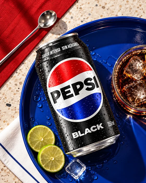 Lata de Pepsi Black en una bandeja azul, con un vaso y rodajas de lima.